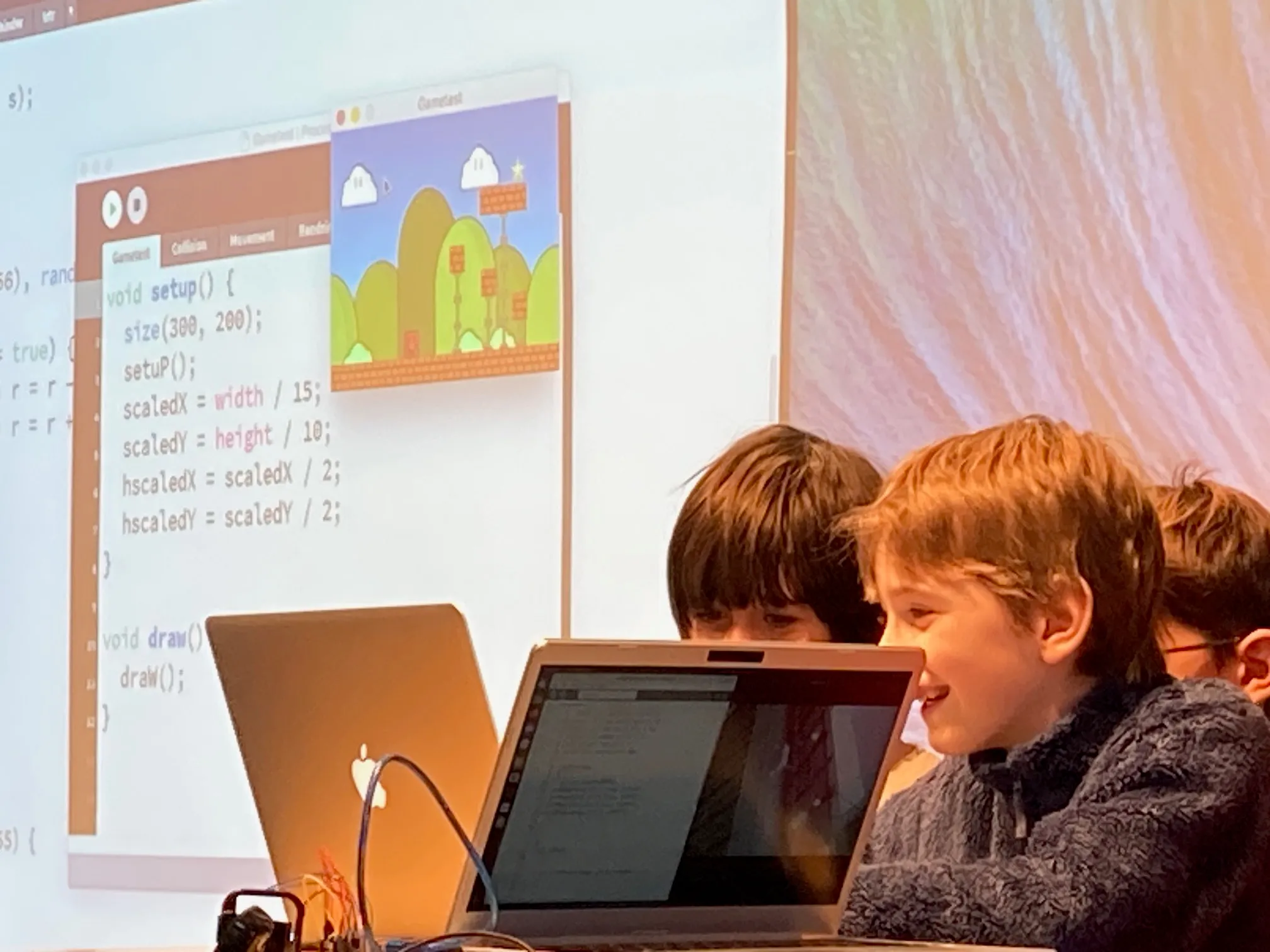 Barn programmerar spel på bärbara datorer framför en projicerad kodskärm.